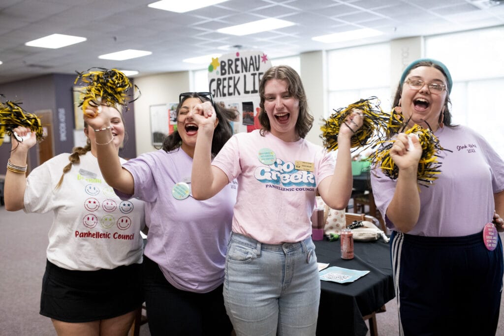 Four student leaders cheer with pom-poms at orientation.