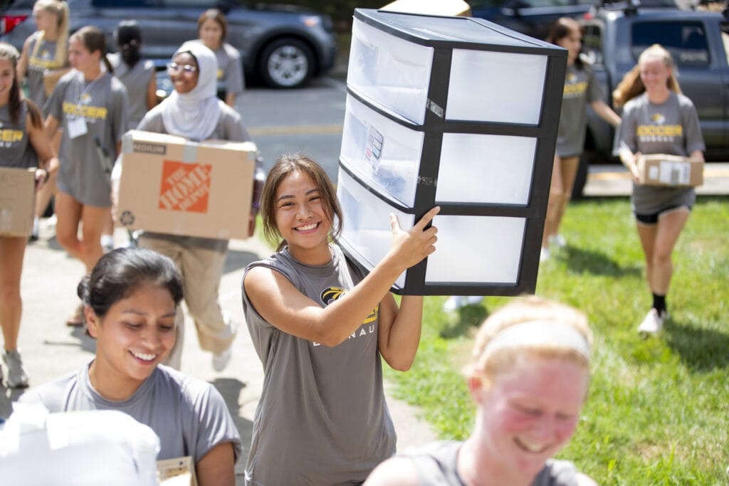 A member of the soccer team smiles as she carries a student's three-drawer organizer