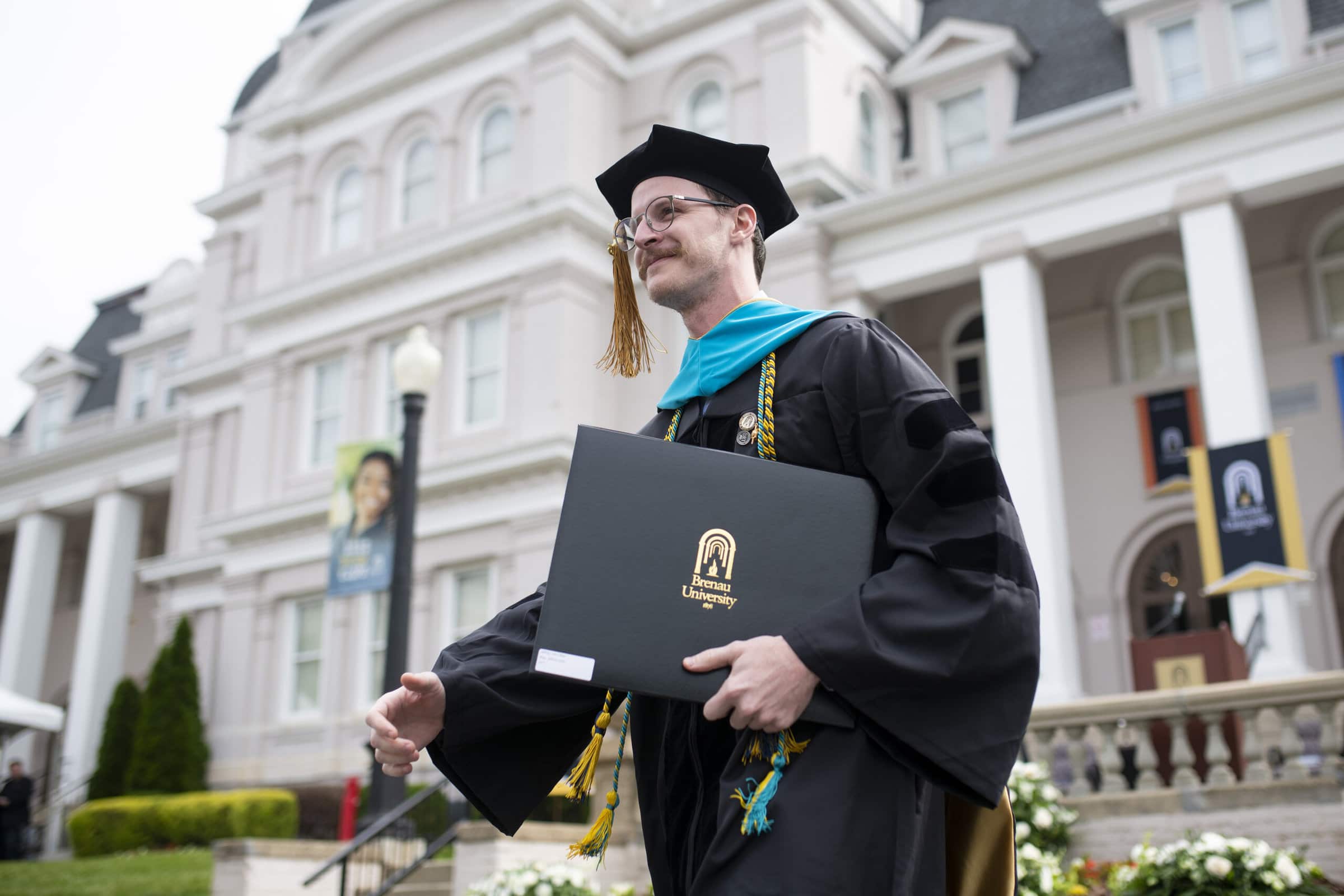 A graduate with his diploma in front of Pearce Auditorium