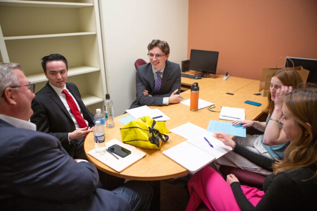 A group of students talk around a table with an evaluator