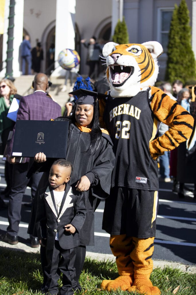 A woman and child pose with her diploma and the mascot, HJ.