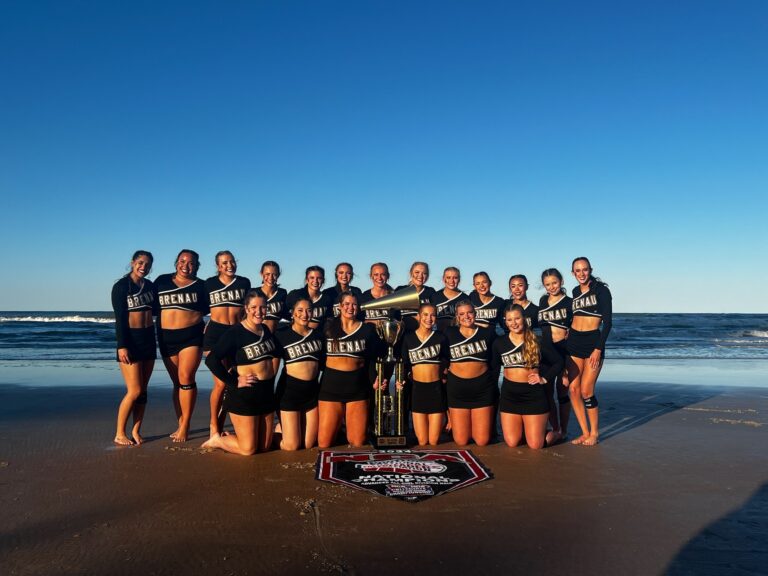 competitive cheer team poses on the beach with title banner