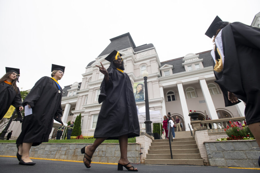 A graduate flashes a peace sign as she walks in front of Pearce during the 145th commencement