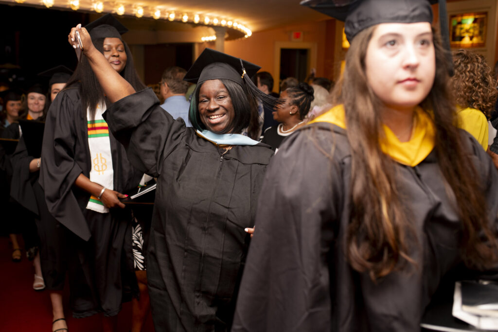 A graduate poses excitedly for a photo while walking down the rows of Pearce