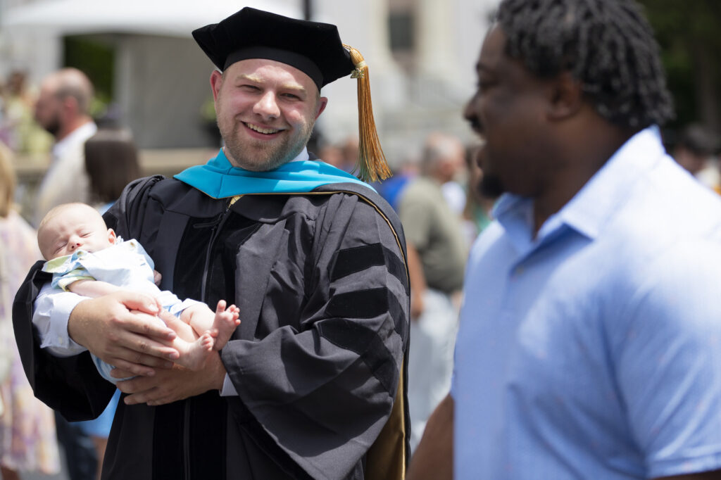 A doctoral graduate holds his infant son after the 145th commencement