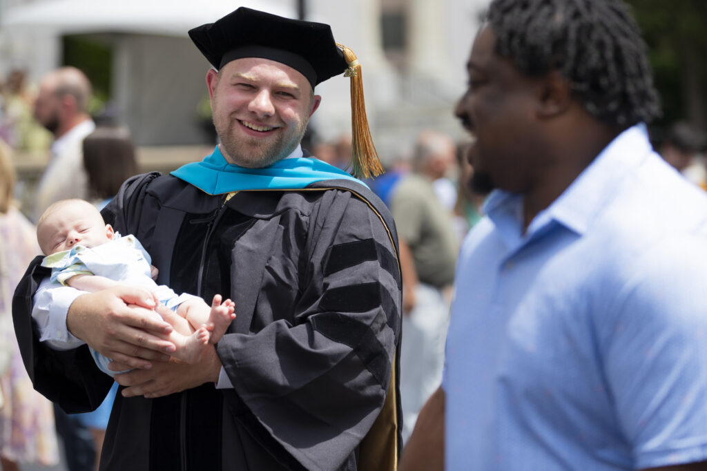 A doctoral graduate holds his infant son after the 145th commencement