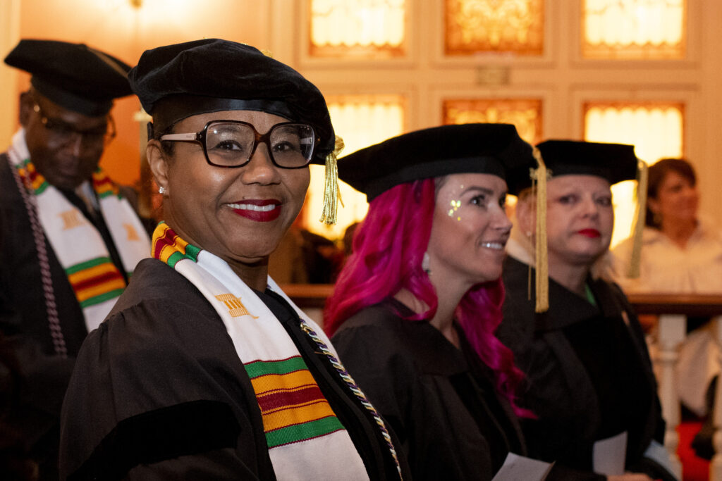 A graduate with glasses smiles at the camera