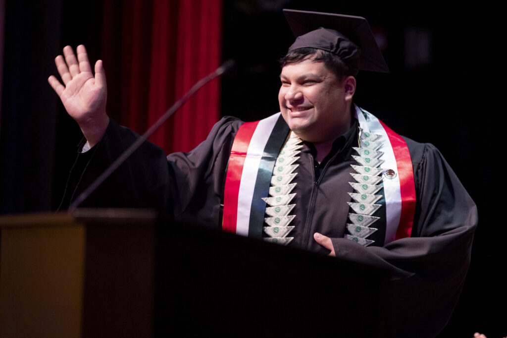A male undergraduate student waves at the crowd