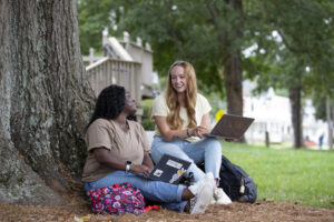 two students with laptops on the front lawn