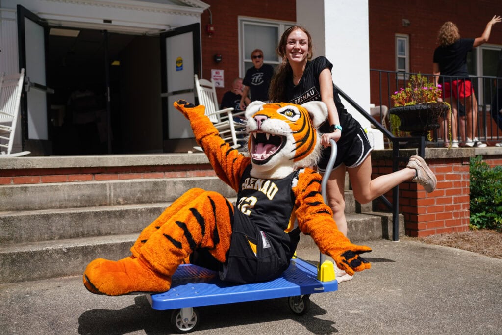 a returning student athlete pushes HJ the tiger on a cart