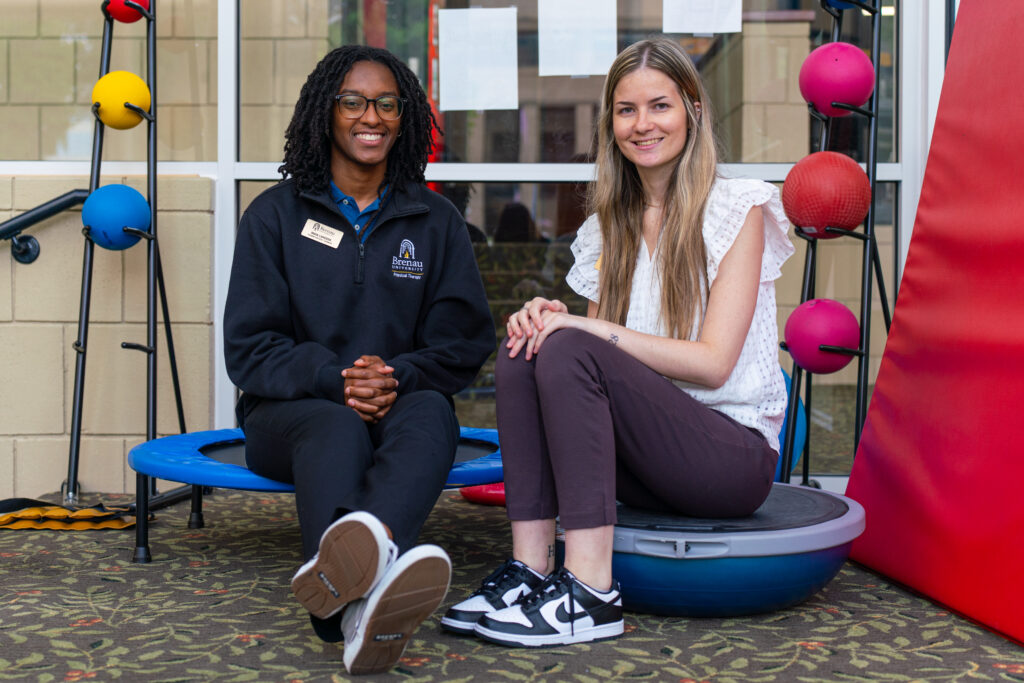 Maya Langdon and Cassidy Hray sit in one of the PT clinic areas with PT equipment