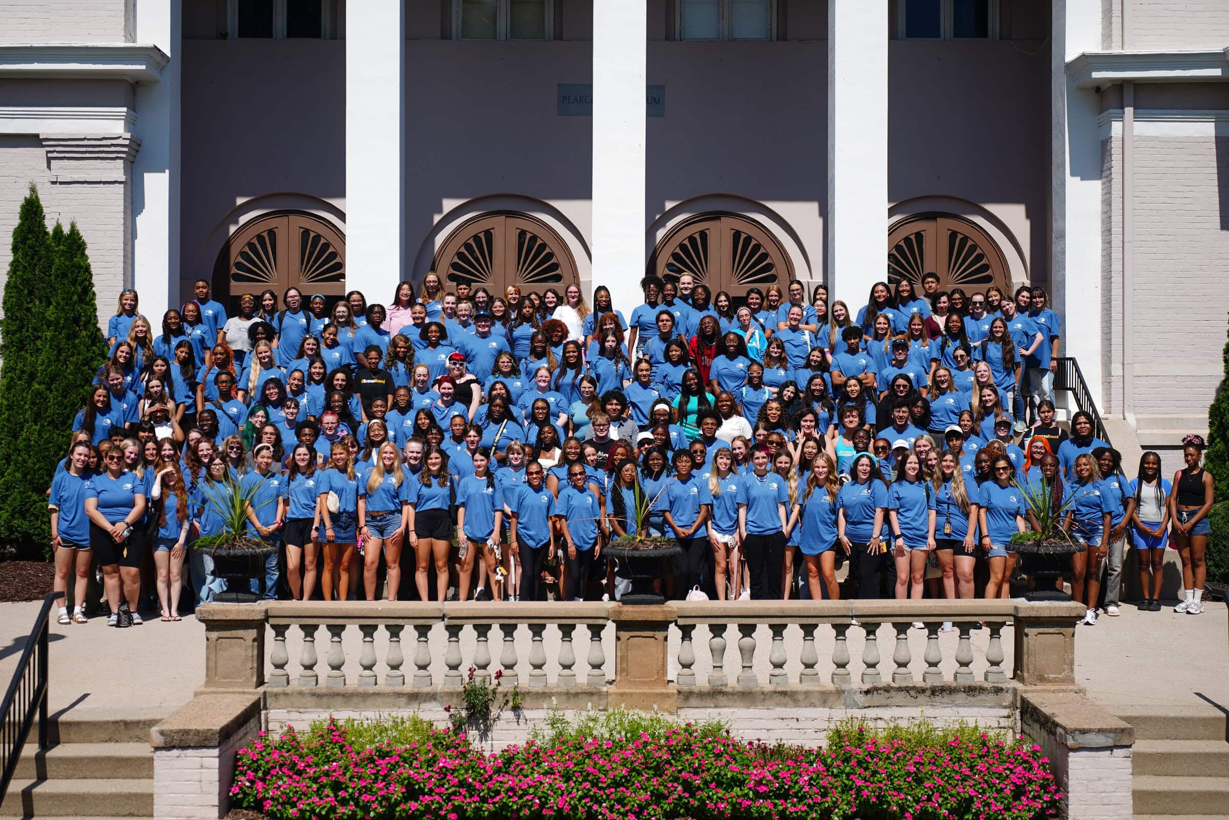 students in blue shirts pose in front of building with columns