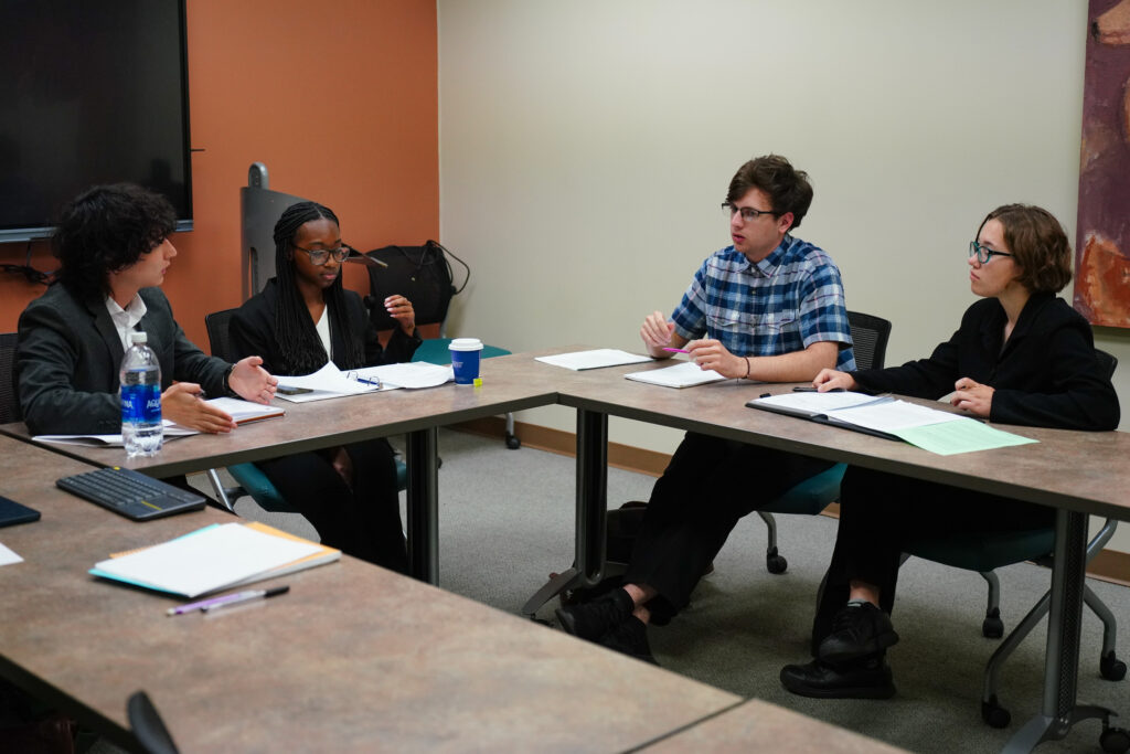 four students at two long tables mid-debate