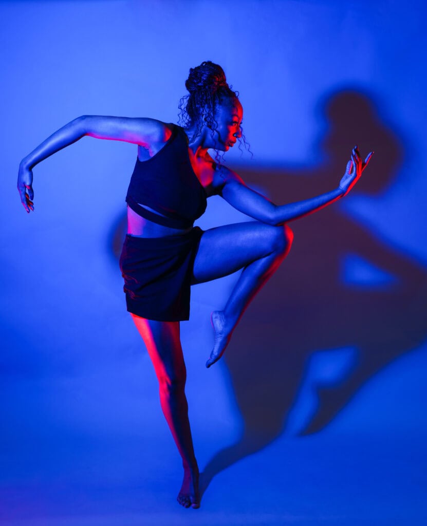 Elegant dancer in vibrant blue and red lighting showcasing movement and flexibility at Brenau University.