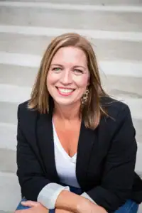 Friendly woman smiling, seated outside on concrete stairs, representing Brenau University student or faculty.