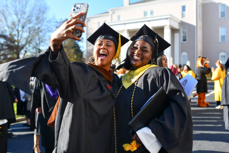 Two women in graduation regalia take a selfie