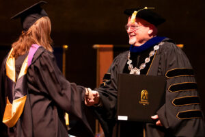 university president in official regalia congratulates and hands diploma to graduate