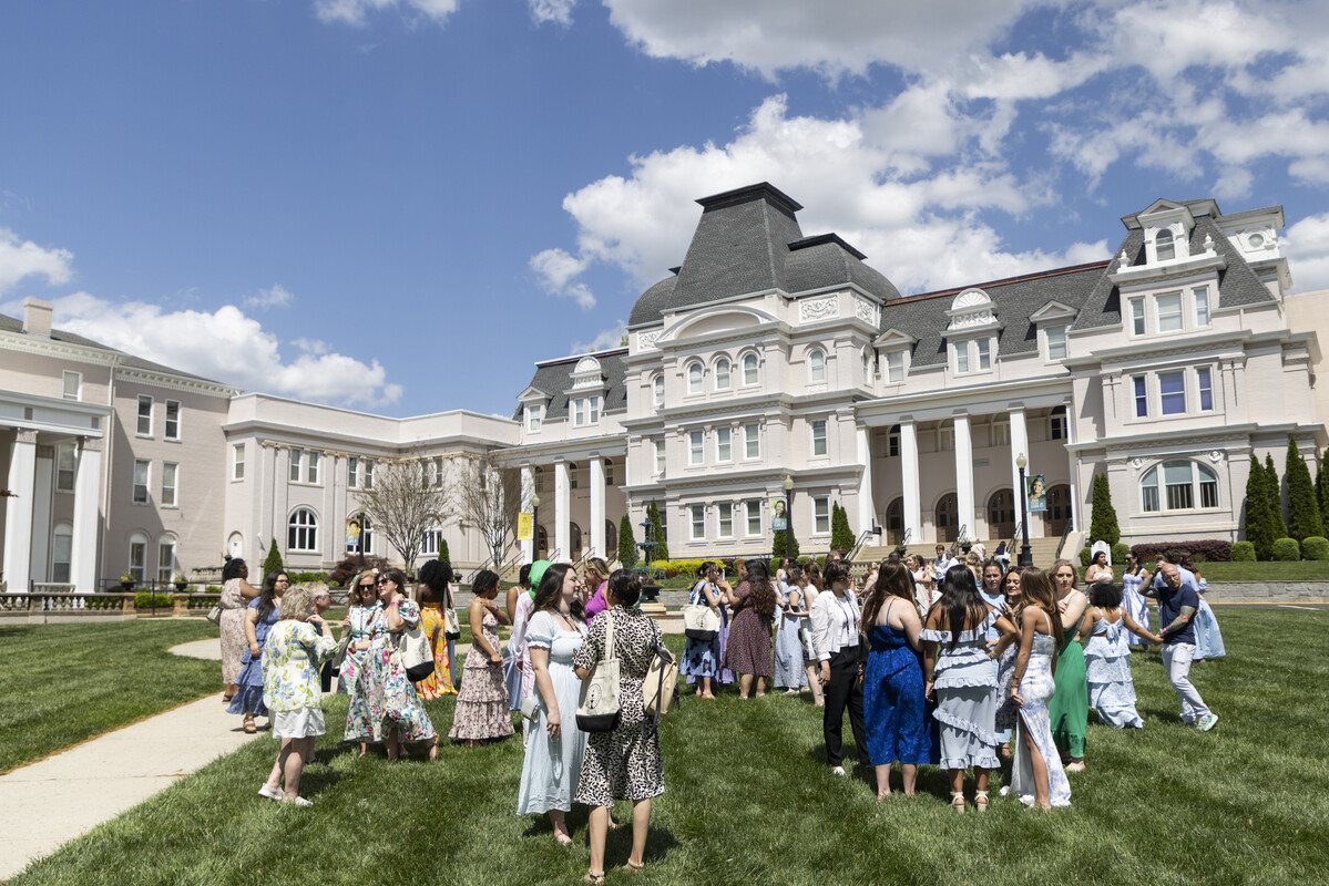 women in spring dresses on a green lawn in front of a university building.