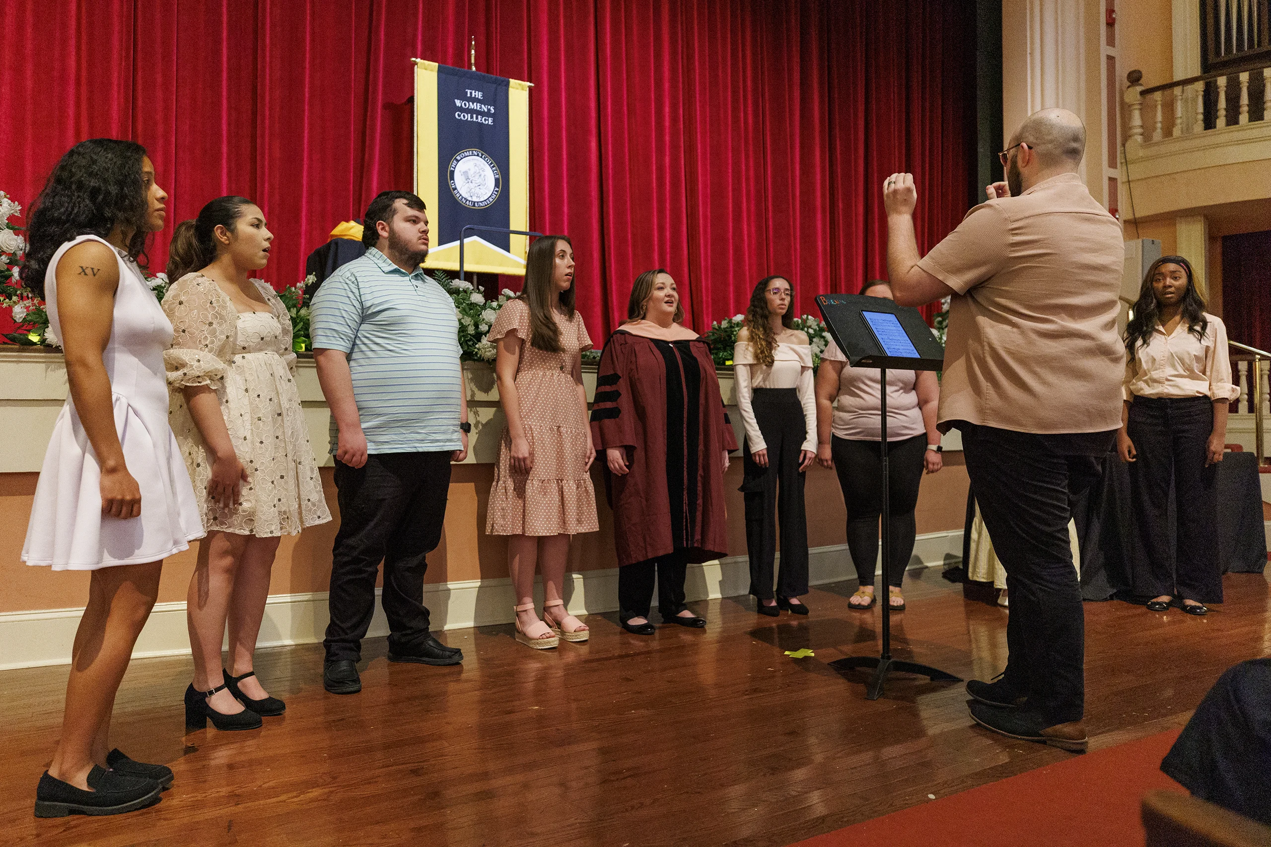 Person conducts singers in front of college gonfalon