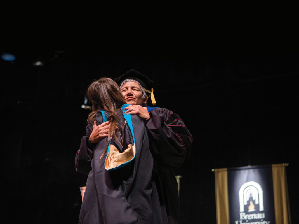Irma Alvarado hugging a student during hooding ceremony.