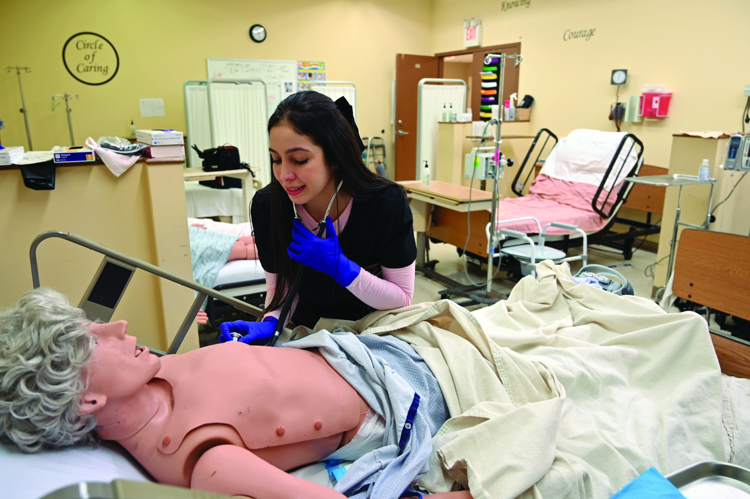 Laura Trimboli, a nursing student, holds a stethoscope close to a dummy laying on a hospital bed.