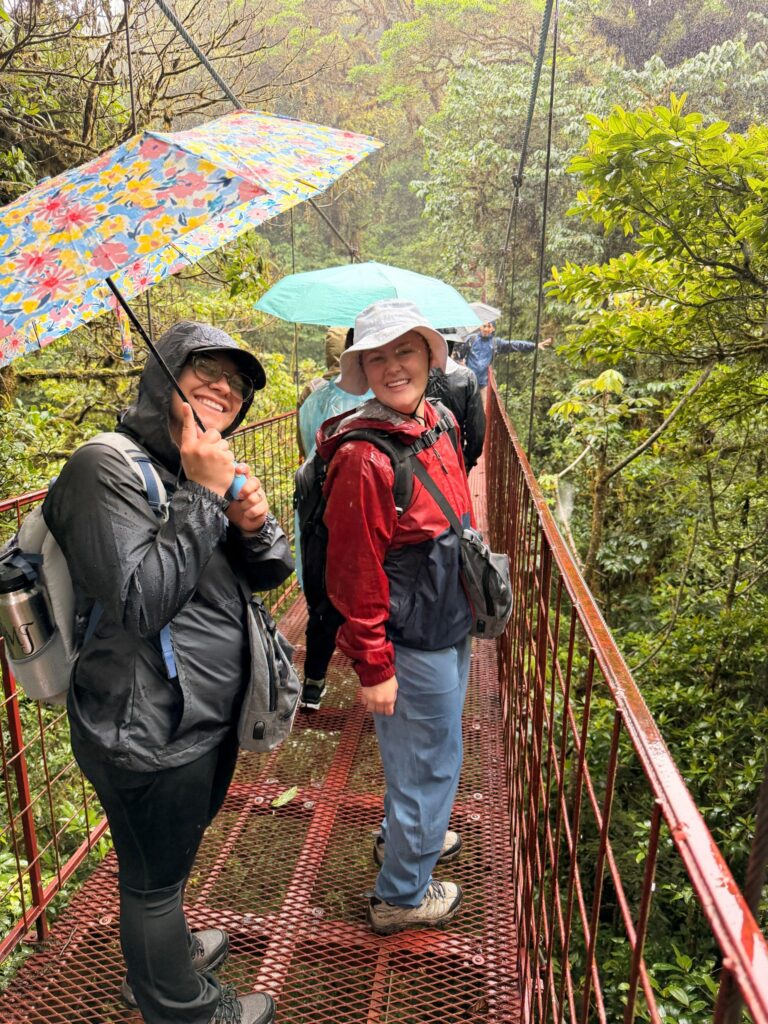 students on bridge in rain forest with umbrella