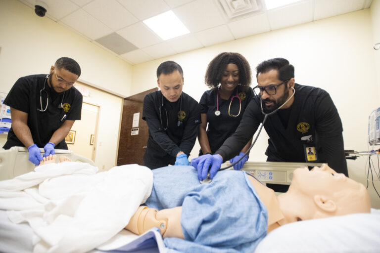nursing students in black scrubs gather around a manikin in a healthcare simulation lab