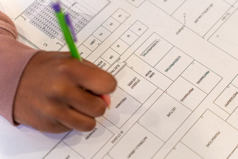 a hand holding a pencil writes on a floor plan for an athletic facility