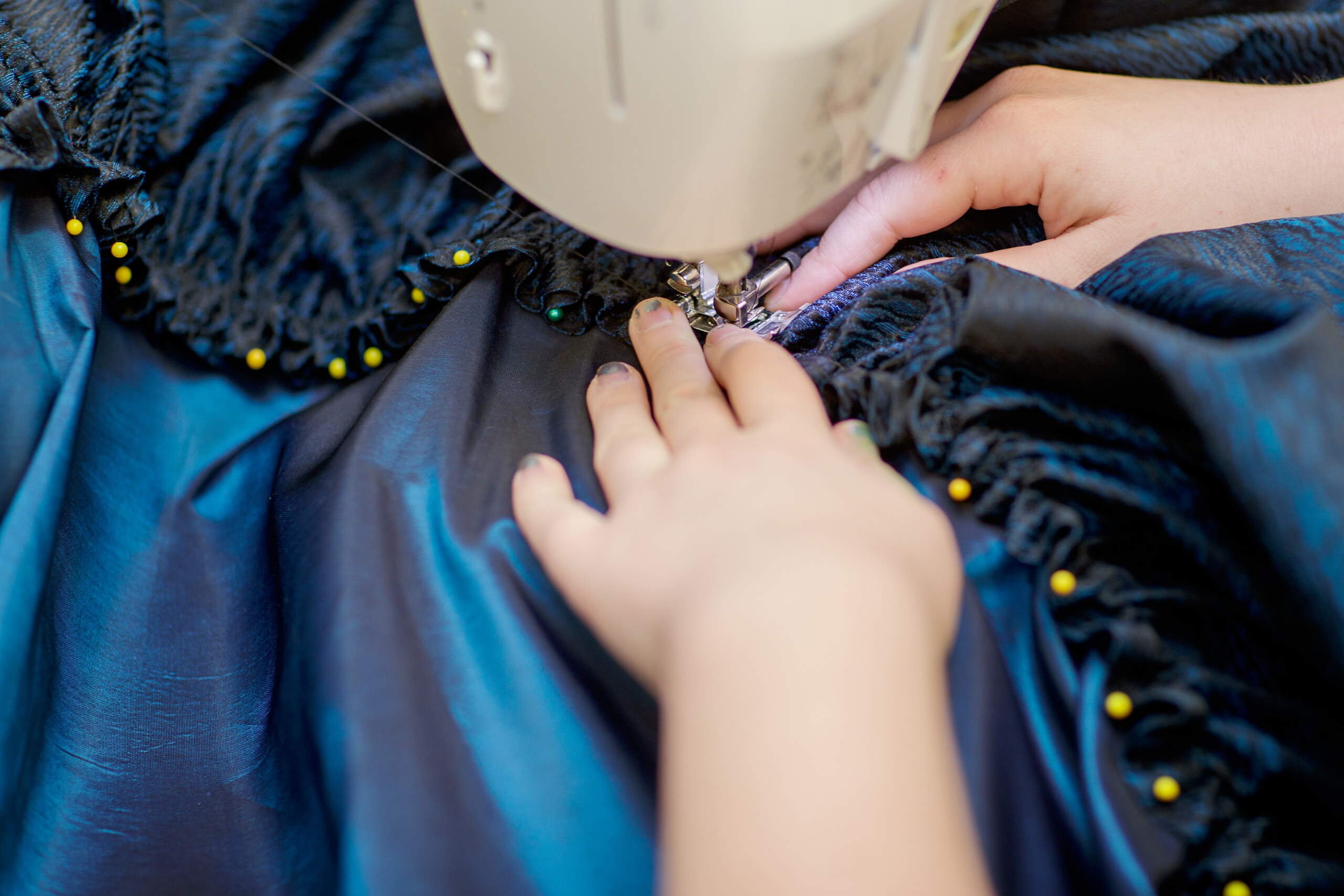 a pair of hands guide shiny blue fabric through a sewing machine.