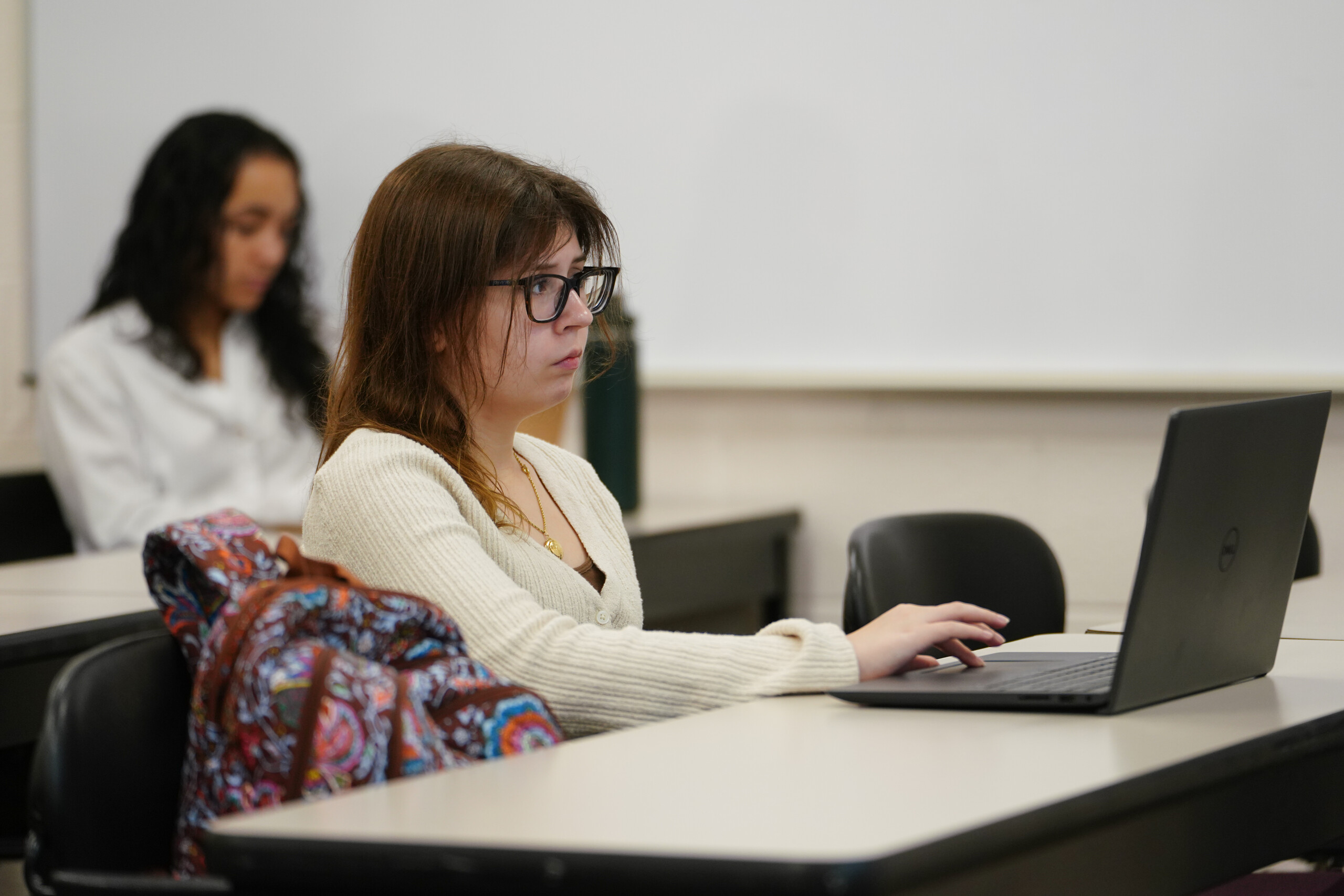College student sits at an open laptop in a university classroom